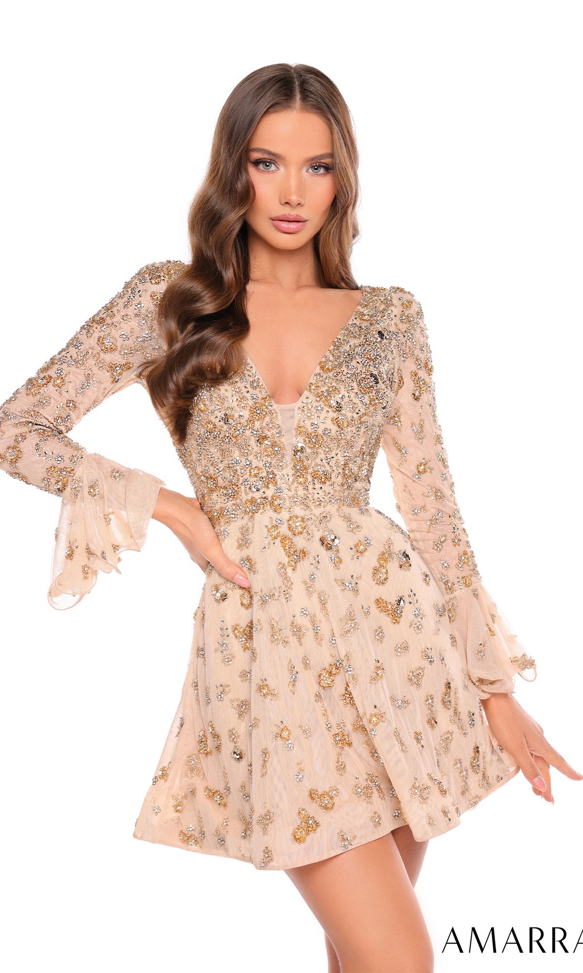 A woman poses with one hand on her hip in the Short Homecoming Dress 88032 by Amarra, a beige mini dress with long sleeves and intricate gold and silver sequin embellishments.